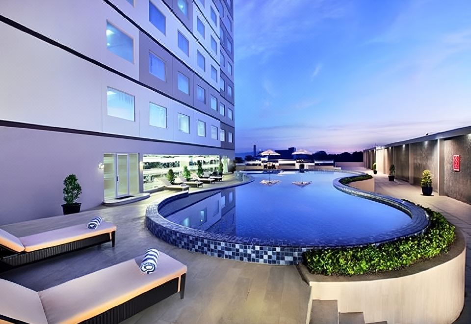 a modern hotel with a large pool , surrounded by comfortable seating areas and a well - lit outdoor area at Aston Karimun City Hotel