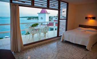 a bedroom with a large window overlooking the ocean , featuring a bed and a dining table at Hotel Laguna Bacalar