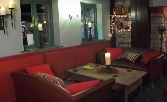 a cozy living room with red couches , wooden tables , and a candle , lit by string lights at The Seven Stars