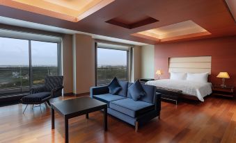 a modern hotel room with wooden floors , large windows , and comfortable furniture , including a blue couch and a black table at Le Meridien Coimbatore