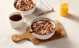 two bowls of granola on a wooden cutting board , accompanied by a cup of coffee and a glass of orange juice at TownePlace Suites Detroit Belleville