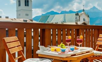 a wooden table with a white plate and two glasses of drinks is set on a balcony overlooking mountains at Royal Hotel Cortina