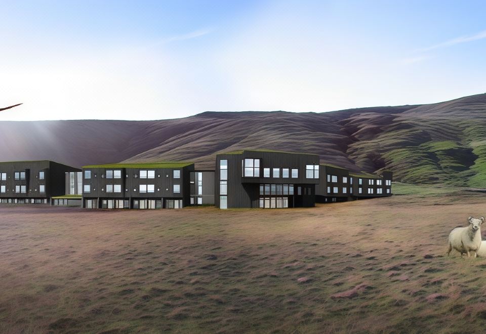 a modern building with large windows is situated on a grassy field , surrounded by mountains at Fosshotel Glacier Lagoon
