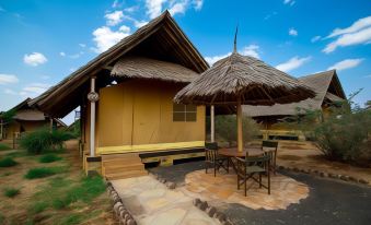 a small wooden house with a thatched roof and a table and chairs under a thatched roof at AA Lodge Amboseli