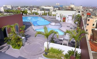 a rooftop pool area with palm trees and chairs , surrounded by buildings in the background at Golden Flower by Kagum Hotels
