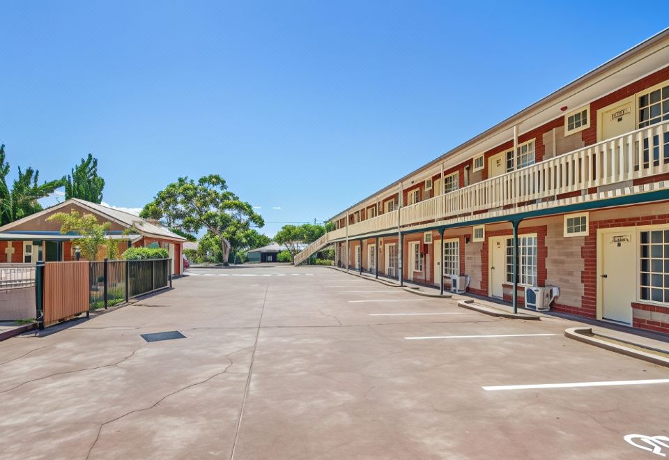 a long , empty parking lot in front of a two - story building with red brick exterior and white railings at Motel Goolwa