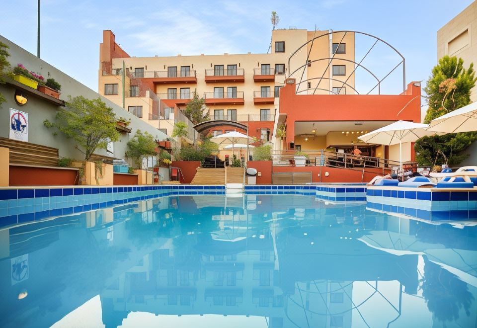 an outdoor swimming pool surrounded by a hotel building , with several people enjoying their time in the pool at Grand Hotel Madaba