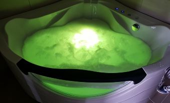 a white bathtub filled with green water and bubbles is illuminated by a light source at Hotel River