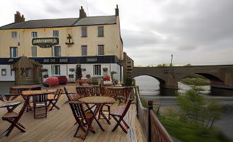 a restaurant with wooden tables and chairs , a bridge in the background , and a large building on a riverside at Anchor Hotel