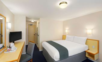 a hotel room with a large bed , desk , and chair , along with a tv in the corner at Days Inn by Wyndham Sutton Scotney South