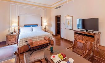 a hotel room with a king - sized bed , a flat - screen tv , and a dining table with fruit at The Oberoi Grand Kolkata