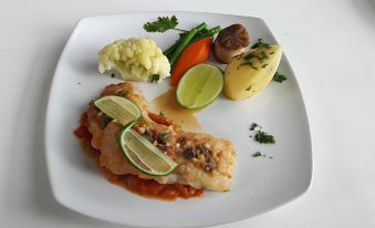 a white plate with a piece of fish on top of a bed of mashed potatoes , accompanied by a variety of vegetables and garnishes at Poonyamantra Resort