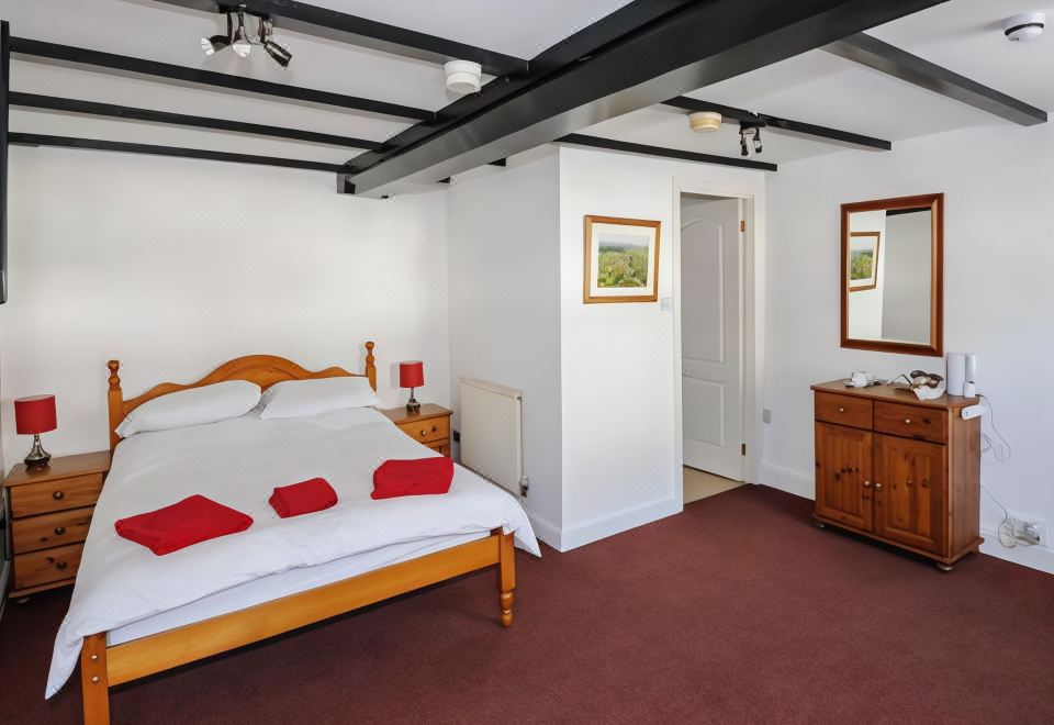a bedroom with a large bed , wooden furniture , and a mirror on the wall , surrounded by white walls at George Inn