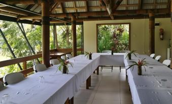 a long table with white tablecloths and chairs is set up in a room with windows at Rainforest Eco Lodge