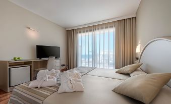 a hotel room with two beds , a desk , and a window overlooking the ocean , as well as towels neatly placed on one of the at Vik Gran Hotel Costa del Sol