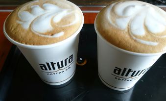 "two cups of coffee with whipped cream on top are sitting on a table , one is labeled "" altura "" and the other is blank" at Anglers Lodge