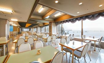 a large dining room with multiple tables and chairs , all facing the ocean , under a cloudy sky at Hotel Urashima