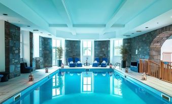 a large swimming pool with blue water and lounge chairs is surrounded by a stone wall at The Atholl Palace