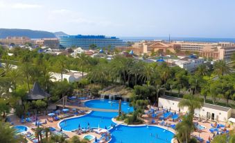 a large swimming pool with blue water and palm trees in the foreground , surrounded by buildings and buildings at Hotel Best Tenerife