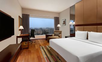 a hotel room with a large window , wooden floor , and white bed , along with two lamps on the nightstands at Courtyard Ahmedabad