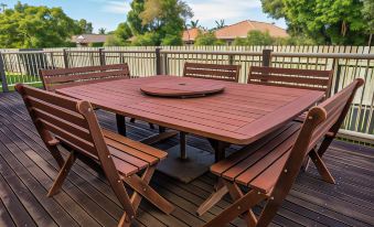 a wooden deck with a dining table and chairs , surrounded by trees and a fence at Aspley Carsel Motor Inn