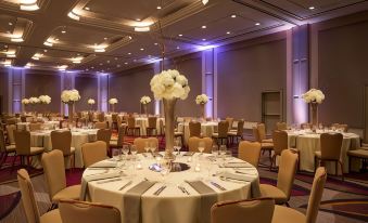 a large , elegant banquet hall with multiple round tables covered in white tablecloths and decorated with centerpieces of flowers at Hyatt Regency Sacramento