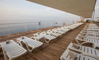 a large wooden deck on the deck of a cruise ship , with numerous white lounge chairs arranged along its length at Falcon Hotel