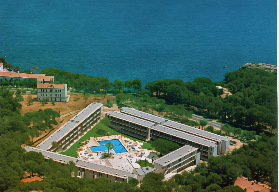 aerial view of a hotel surrounded by trees and a body of water , with a pool in the center at Aparthotel Comtat Sant Jordi
