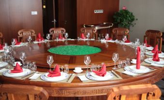 a large round wooden dining table set with red napkins , wine glasses , and a green centerpiece at Spring Hotel