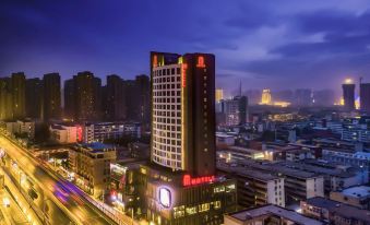 a tall hotel building surrounded by a city at night , illuminated by street lights and cars on the road at M Hotel