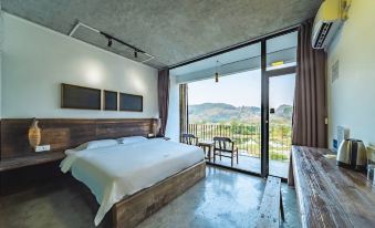 The bedroom features large windows and a balcony that overlooks the mountainous region, with an unmade bed and a cluttered desk filled with scattered papers and books at Yangshuo Sudder Street Guesthouse
