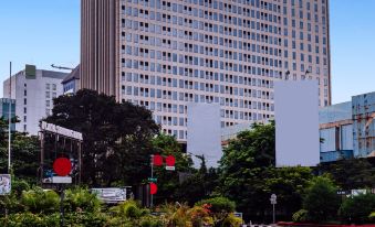 a large white building with a red sign on top is surrounded by trees and traffic lights at Louis Kienne Hotel Simpang Lima