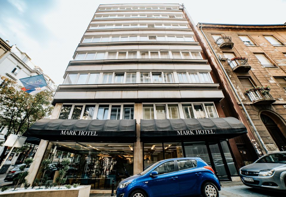 "a blue car is parked in front of a tall building with a sign that says "" mark hotel ""." at Mark Hotel Belgrade