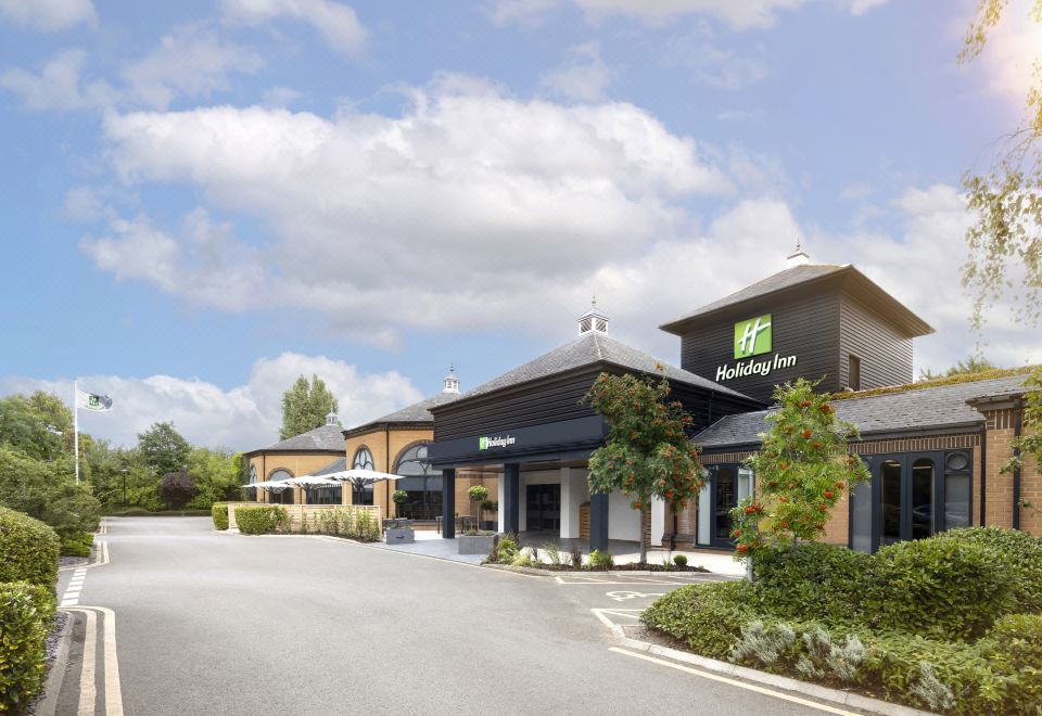 a holiday inn express hotel with a large parking lot in front of it , surrounded by trees at Holiday Inn Gloucester - Cheltenham