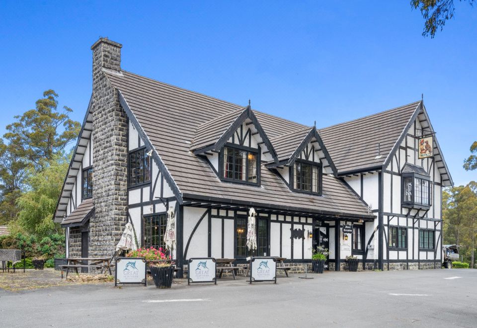 a large , black and white building with a gray roof and a stone chimney is situated in front of trees at The Fox and Hounds Historic Hotel