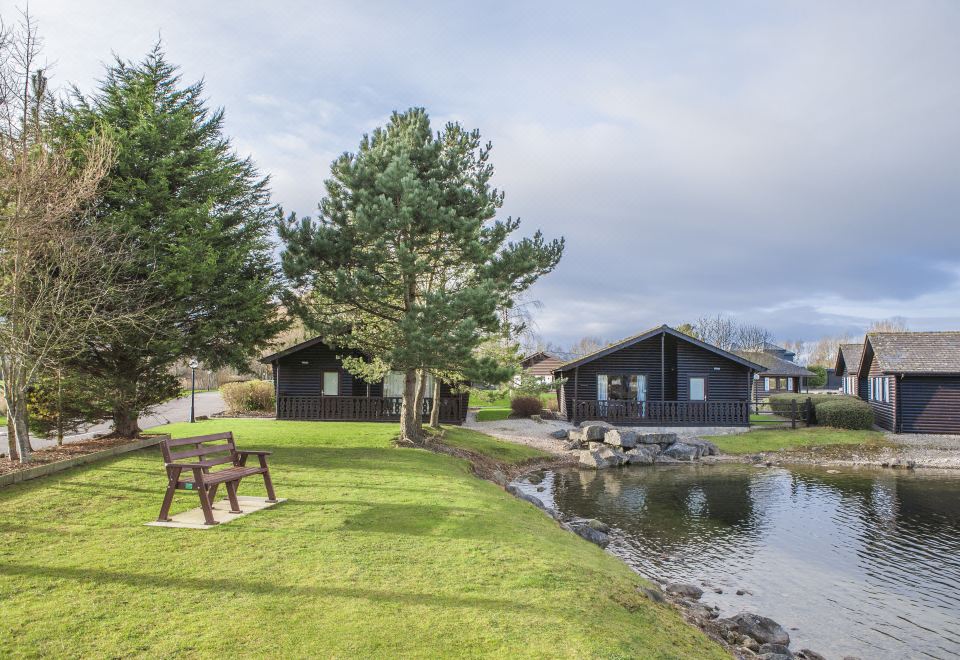 a serene scene of a wooden cabin situated near a lake , surrounded by green grass and trees at Pine Lake Resort