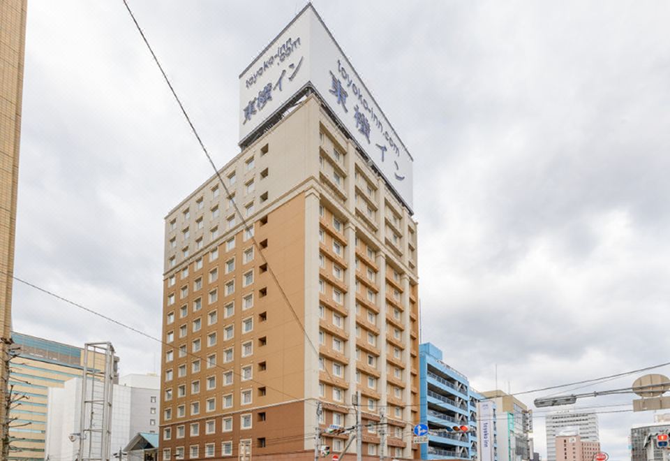 a tall building with a blue sign on top is surrounded by other buildings in the city at Toyoko Inn Oita Ekimae