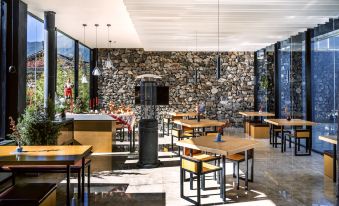 a modern restaurant with wooden tables and chairs , large windows , and a stone wall background at The Rock Hotel