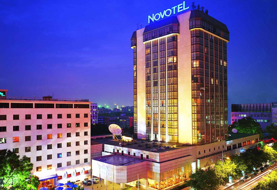 A photo of a large building with city lights in the foreground taken at night at Novotel Beijing Peace