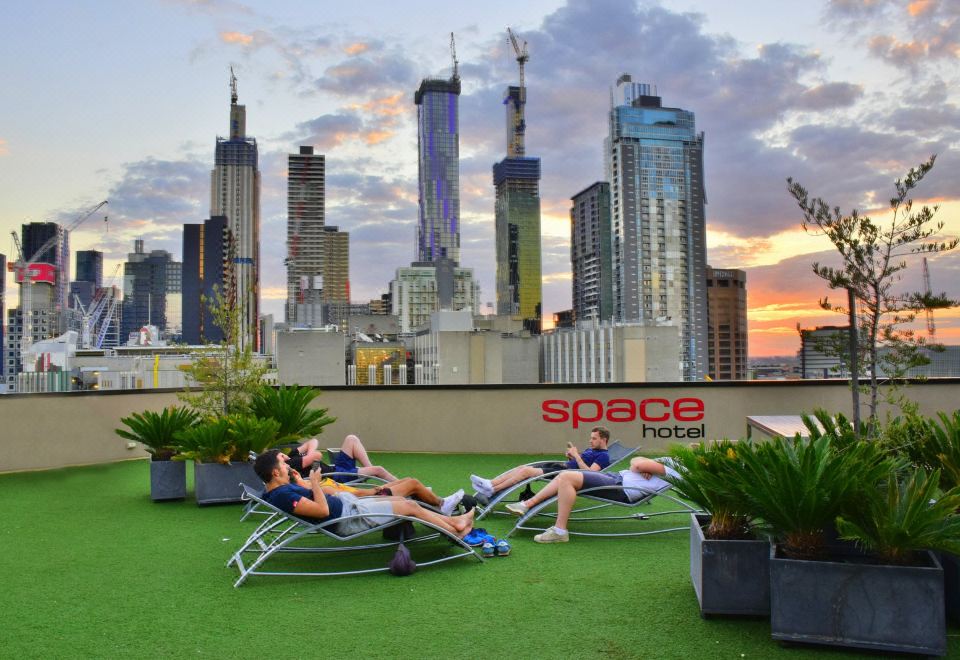 a group of people relaxing on lounge chairs on a rooftop with a city skyline in the background at Space Hotel