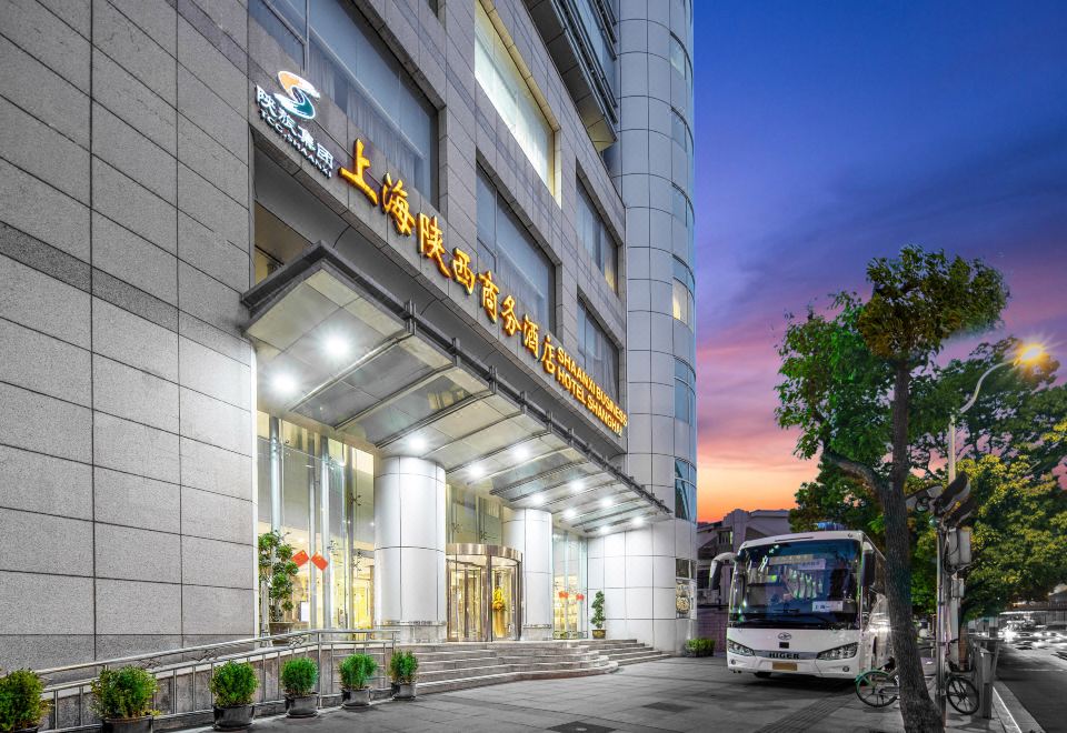 The front entrance of a hotel is shown with a view of the surrounding business buildings in the background at Shanghai Shaanxi Business Hotel