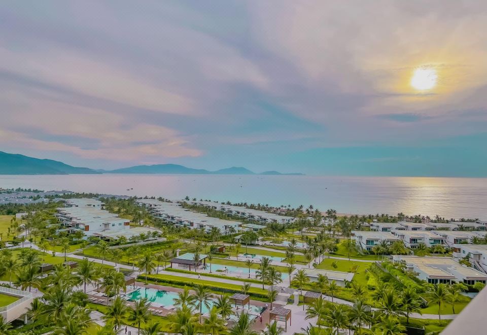 aerial view of a resort with a pool surrounded by palm trees , a golf course , and a body of water at Alma Resort Cam Ranh