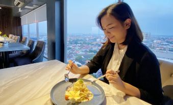 a woman in a business suit is sitting at a dining table with a plate of food in front of her at Louis Kienne Hotel Simpang Lima