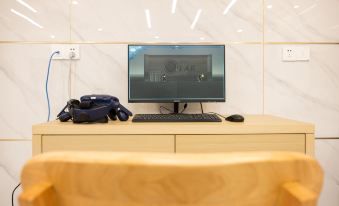 A computer monitor is placed on top of a desk, alongside an empty wooden chair and keyboard at Guangmingding Hotel