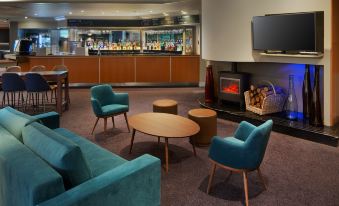 a hotel lobby with a fireplace , a bar , and several chairs arranged around it for guests to sit and relax at DoubleTree by Hilton Manchester Airport