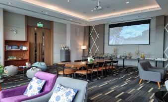 a modern lounge area with a wooden table , chairs , and a large screen on the wall at Grand Fortune Hotel Nakhon Si Thammarat