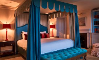 a bed with a blue canopy and white sheets is in a room with a blue bench at Small Luxury Hotels of the World - the Mitre Hampton Court