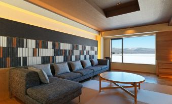 a living room with a gray couch , wooden coffee table , and large windows overlooking the ocean at Lake Akan Tsuruga Wings