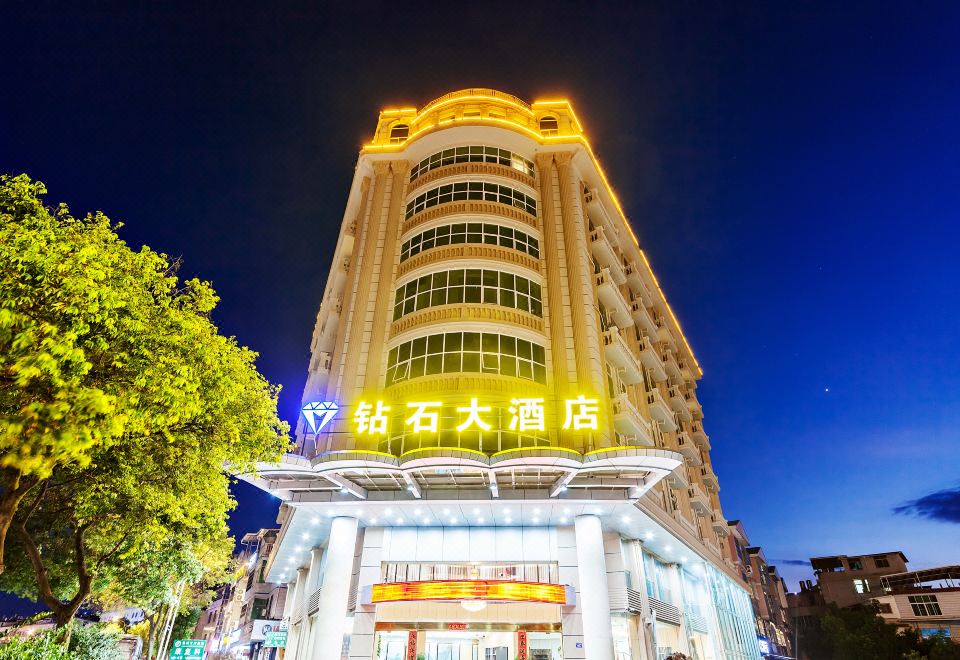 a tall building with a large sign on the front , illuminated at night against a dark sky at Diamond Hotel (Liancheng Guanzhishan Airport)