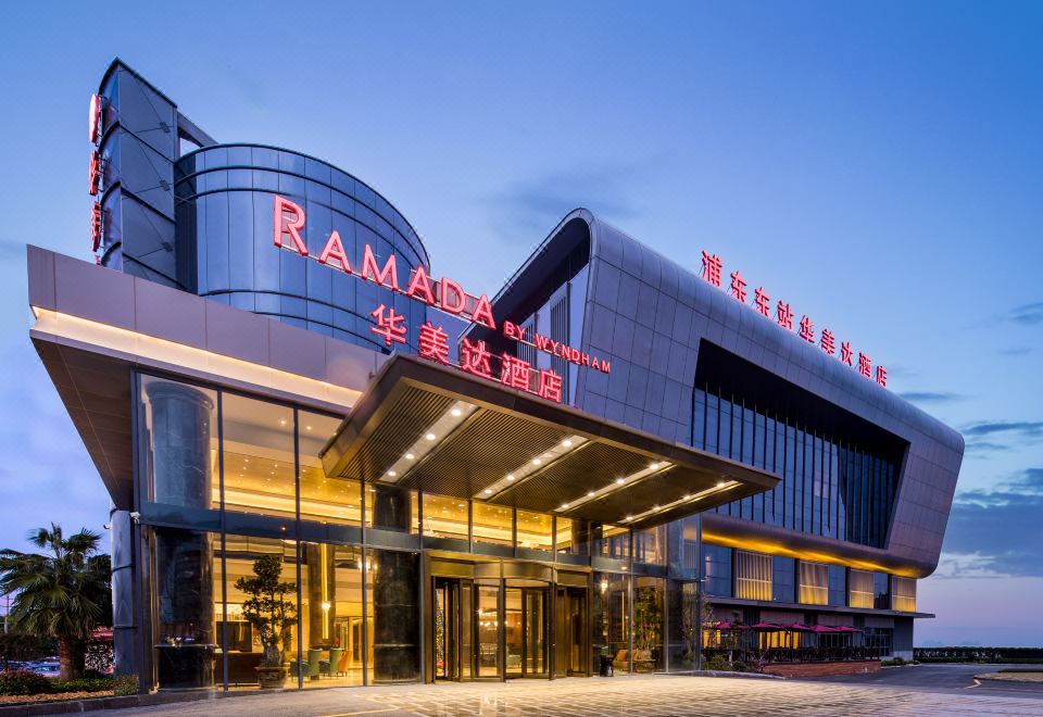 The front entrance of a hotel in an urban setting features large glass and steel doors at Ramada Shanghai Pudong International Airport East Station